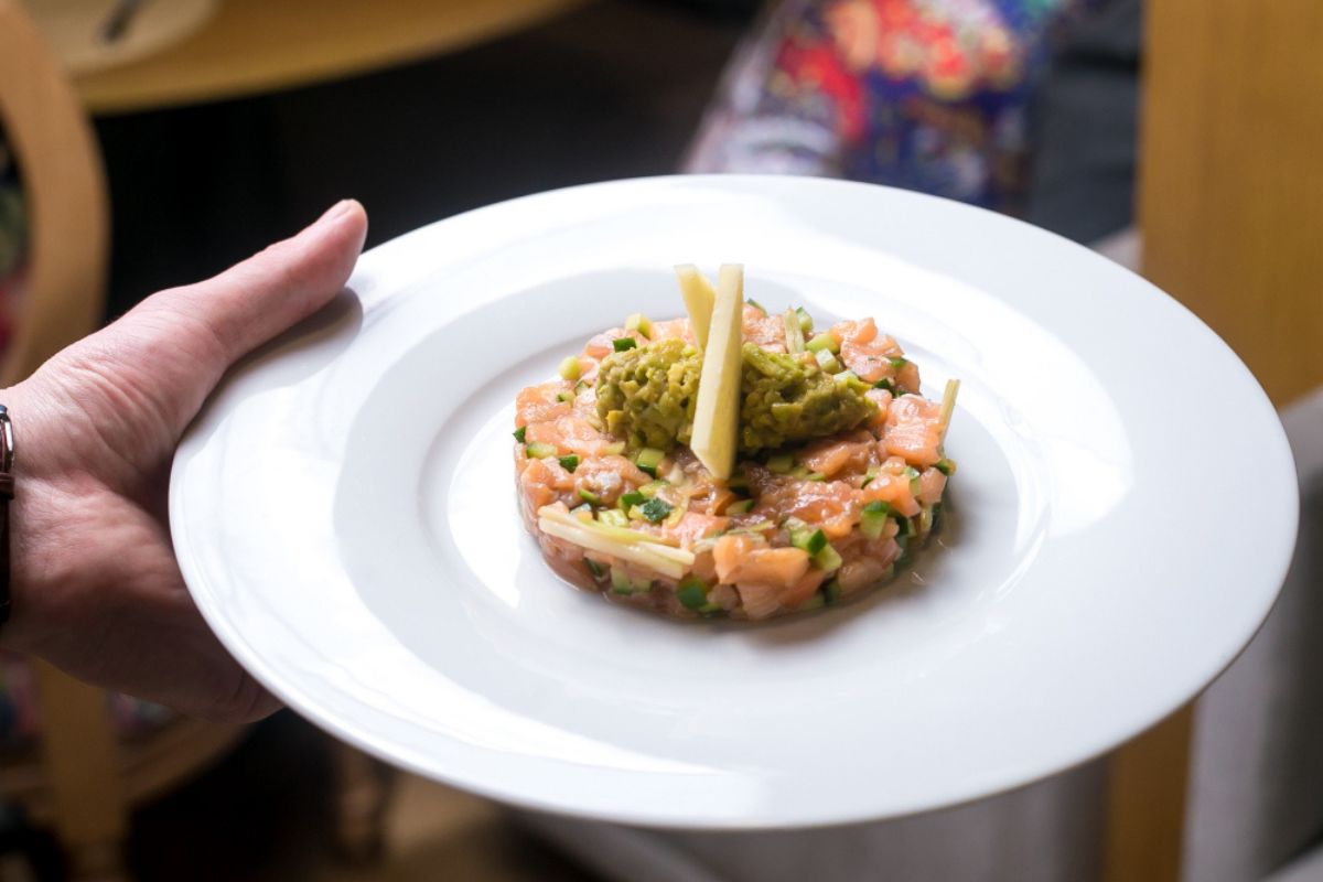 Un camarero sostiene un plato de tartar con verduras 