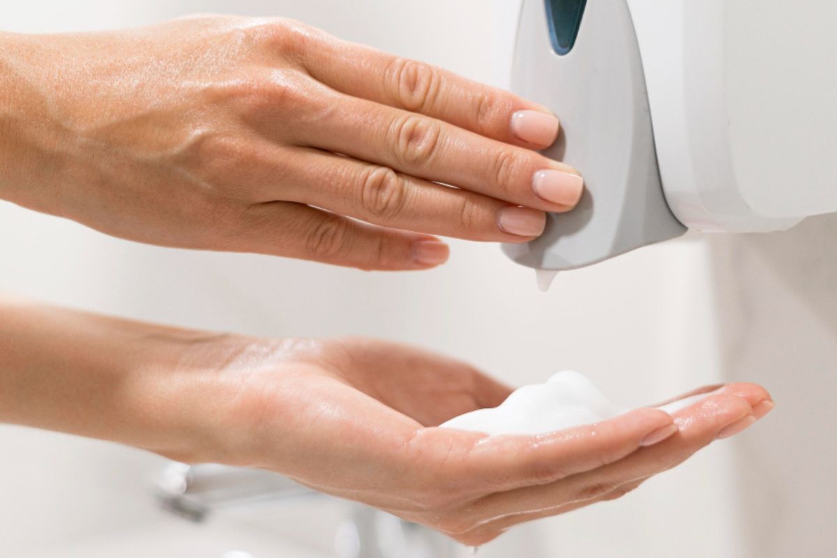 Una mujer se echa jabón en las manos empleando un dispensador en un baño