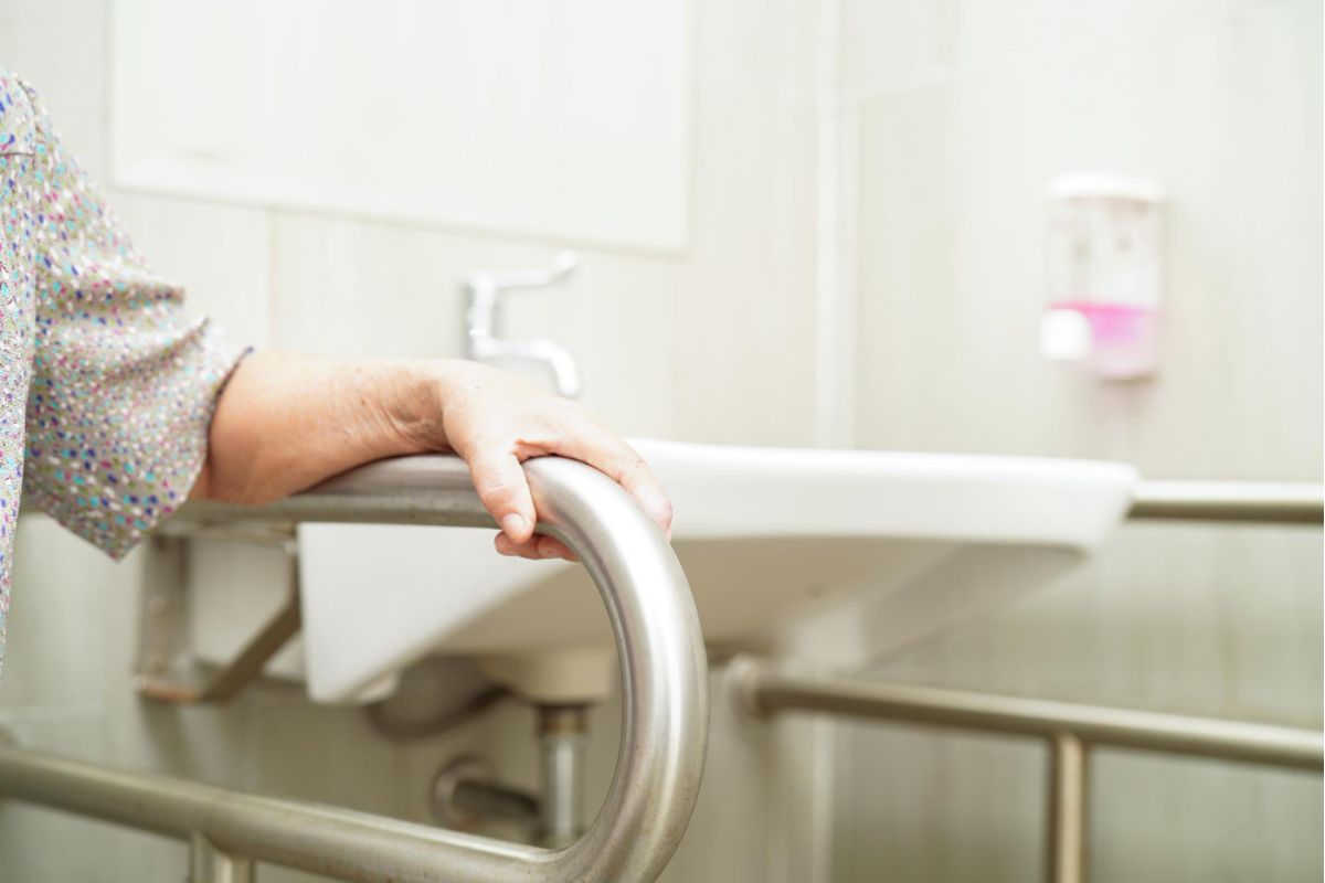 El brazo de una mujer se sujeta sobre una estructura en un baño adaptado para personas con movilidad reducida