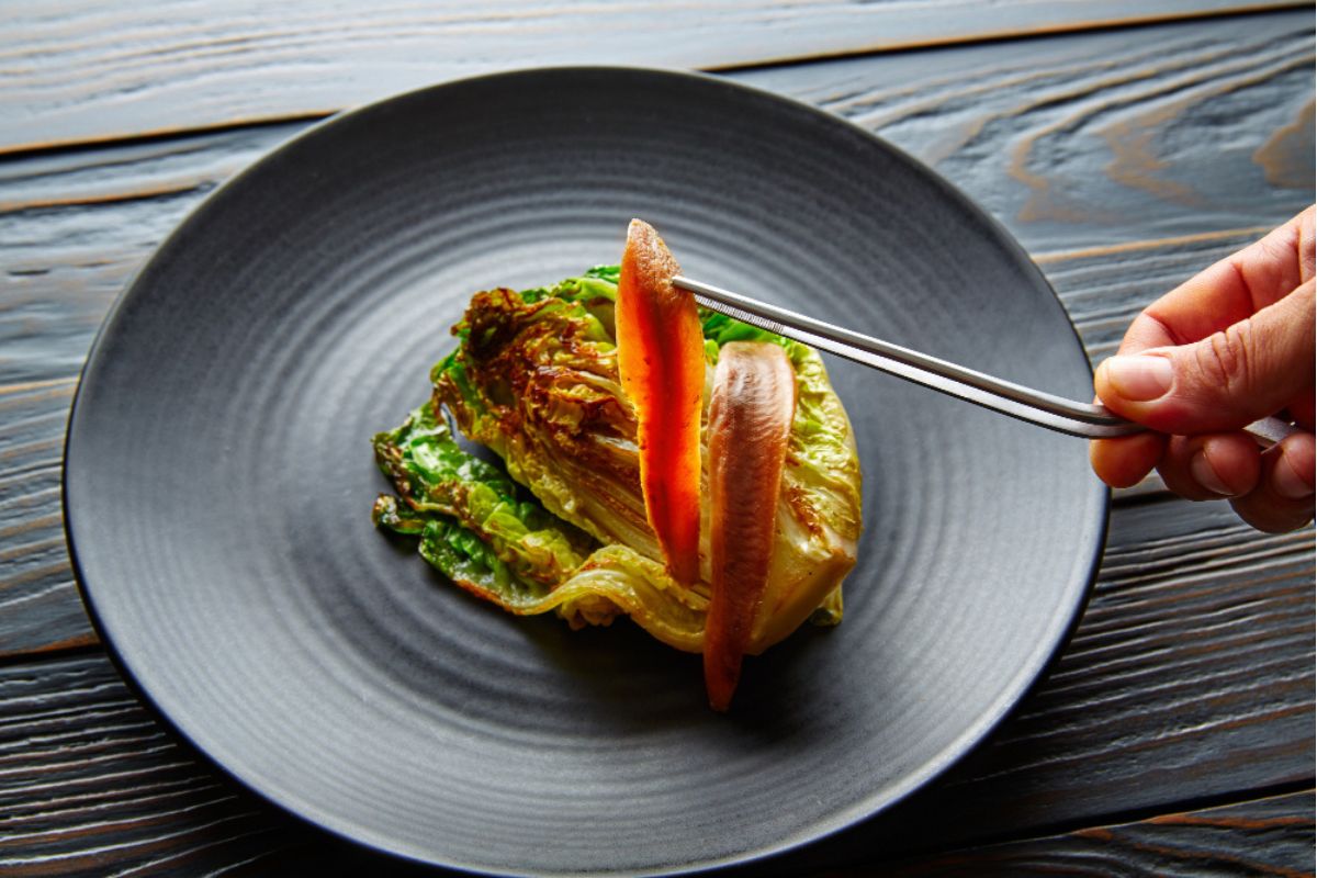 Una Mano Emplata Unas Anchoas Sobre Un Plato De Cogollos Braseados